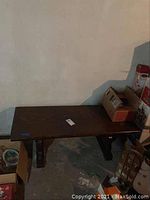 Rectangular wood coffee table placed on basement floor next to wall, surrounded by boxes and other items.