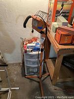 Two orange work lights on stands with protective guards near a plastic Sterilite storage drawers and light bulb boxes in a basement corner.