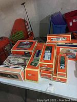 Multiple Lionel-branded orange boxes on table, showing various train cars and accessories.