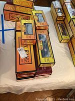 Multiple original boxed Rail King by MTH Electric Trains die-cast model trains and freight cars arranged on a table, showing the orange and yellow branded boxes with labels and clear display windows.