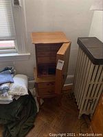 Wooden jewelry armoire positioned against a wall, drawers and door open to reveal storage compartments and hanging necklaces