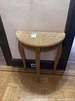 Front view showing the half-moon wicker top and three wooden legs, placed against a wall corner.