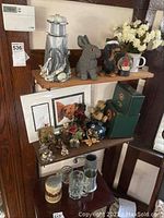 Shelf with Boyd's Bears figurines, lighthouse figurine, gray rabbit, snow globe, faux flowers, framed bear art, glass steins, and plush bears visible.