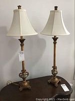 Two matching buffet lamps on a dark wood surface with white linen-like shades and ornate gold-silver bases.