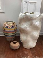 Three vases together: a colorful patterned large ceramic vase, a small round sandy textured pottery vase, and a tall irregular white ceramic vase.