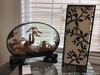 Both lamp with metal frame and linen-like shade alongside Asian cork carving on wooden base shown on glass table near window blinds.