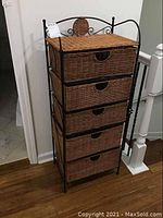 Full front view of tall chest showing five wicker drawers within black metal frame on hardwood floor.
