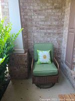 Full view of metal wicker swivel chair with green cushions and a daisy pillow on front porch