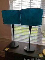 Two turquoise velvet shade floor lamps standing side by side showing full lamp height and bases.
