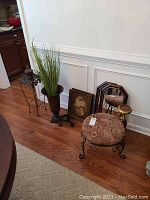 Wide view showing multiple items including the tall metal vase with artificial plant, framed print, stool, mirrors, candle holder, and stand.