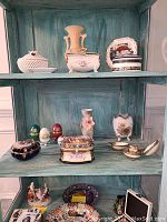 Photo of three shelves filled with various Limoges porcelain pieces including vases, egg-shaped objects, decorative boxes and plates.