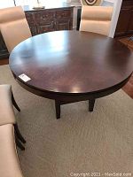 Round wood dining table with smooth dark finish seen from above with upholstered chairs around it