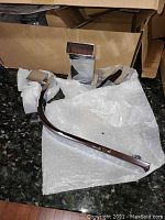 Chrome finish tub and shower faucet lever and parts wrapped in packaging on a granite countertop