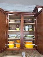 Two-cabinet open front view showing full lot of Pyrex bowls and mugs arranged on four shelves