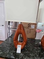 Front view of one brown ceramic base table lamp on black granite countertop, showing its glossy brown geometric base with hollow center and a white rectangular shade.