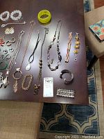 Top-down photo of assorted costume jewelry laid out on a dark wooden table including necklaces, bracelets, and earrings