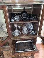 Wooden cabinet shelf showing black hobnail and clear glass pieces