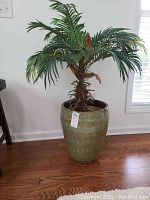 Full view of large green ceramic vase with artificial palm plant inside, showing texture and size.