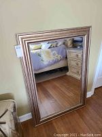 View of entire mirror showing rectangular shape, large size, and decorative wide wooden frame with some metallic bronze finish and distressed look.