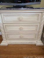 Front view of nightstand showing three drawers, carved detailing and marble top