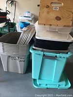 Stack of plastic storage bins of varying sizes and colors with a wooden crate on top, some bins labeled Patio Trap and Plastic Pieces Trap 2018