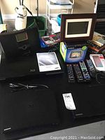 Black Samsung Blu-ray and DVD players, TEAC iPod player, Garmin StreetPilot GPS in box, DVDs and remotes on black table.
