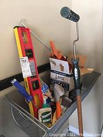 Overview of tools and supplies in a basket showing various brushes, a level, paint roller, and wood glue bottle.