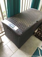 View of closed brown Suncast plastic storage bin with woven texture and side handles