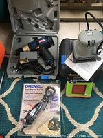 Ryobi drill in case with attached power cord, Porter-Cable sander with manual, Dremel Grout Removal Tool Kit in new packaging with sanding sheets