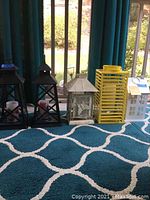 Five lanterns arranged in a row on blue and white patterned carpet, showing the variety of designs and colors including black, cream, yellow, and white.