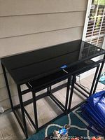Front view of 3 nested black glass-top tables with metal frames on porch floor.