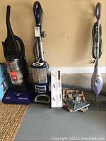 Photo of two upright vacuum cleaners and a steam mop along with WORX Hydroshot accessories on the floor against a wall.