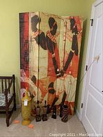 Front view of three-panel room divider featuring stylized African figures, with decorative yellow vase and small figurines positioned in front on the floor.
