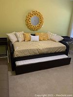 Overall front view of the daybed with trundle extended, showing the faux leather frame, bedding, and pillows arranged on the mattress.
