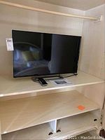 Vizio 32 inch TV placed inside a white cabinet unit with remote and documents under the screen.