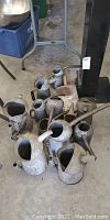 Overview of several vintage oil cans of different shapes and sizes placed on garage floor, showing various states of dents and wear.