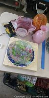 Photo showing Davis Carroll Floral Heirloom decorative plate in box, pink and amber glass vases on table
