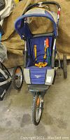 Front view of blue Reebok jogging stroller showing three wheels, hood, and seat with orange harness.