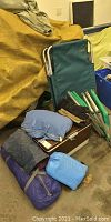 Full camping gear lot including folded tent canvas, cooler, gloves, folded chairs, and air mattresses seen on floor.