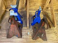 Two pairs of automotive jack stands in wooden crate, one blue and one orange rusted pair