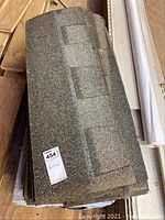 Close-up photo showing reflective granulated surface layers of roofing shingles in open and sealed packages.