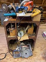 General view of the wooden stand holding manual bench grinder, Black & Decker circular saw, DeWalt drywall screwdriver, Makita drill, various tools and accessories around.