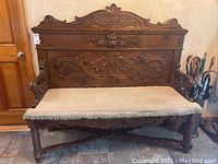 Front view of entire bench showing carved backrest crest, panels, arms, and upholstered cushion