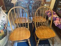 Set of four wooden Windsor style chairs arranged together showing their spindle backs, arched top rails, contoured seat, and turned legs with stretchers.