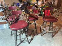 Four vintage bar height swivel stools with burgundy vinyl seats and wooden bases placed on concrete floor