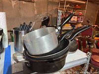 Stacked aluminum saucepan and black frying pans on table with background storage