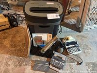 Full view of Royal shredder, keyboard, desk lamp, calculators, printer ink cartridges, and computer case.
