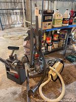 Kirby upright vacuum with a chrome body and cloth vacuum bag alongside Oreck canister vacuum and multiple hose attachments on basement floor.