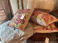 Four embroidered floral throw pillows stacked on the light blue quilted comforter.