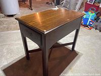 Full view of the wood side table showing top, side drawer, and legs with wear and scratches visible.